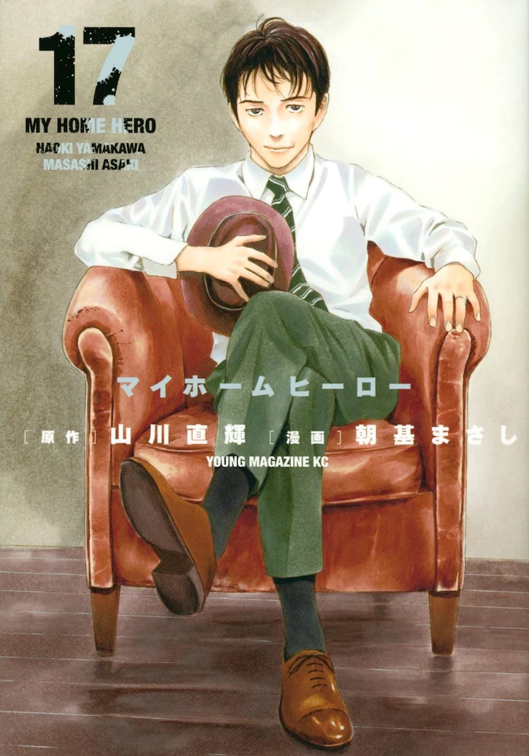 The cover of Volume 17 of the My Home Hero manga, as illustrated by Masashi Asaki. The cover features the main character, Tetsuo Tosu, sitting in a stuffed leather chair in a room with hardwood floors. Tetsuo sits with his legs crossed and his hat clutched to his chest. He wears a white long-sleeved business shirt, a green tie with a stripe pattern, light green slacks, and brown loafer shoes. He has a half-smiling, half-ambivalent expression upon his face.