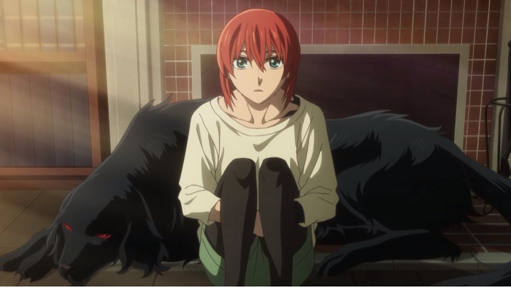 Seated on the kitchen floor and leaning against her familiar, the churchgrim Ruth, Chise is surprised to learn that she'll be heading to a magical university in a scene from the upcoming second season of The Ancient Magus' Bride TV anime.