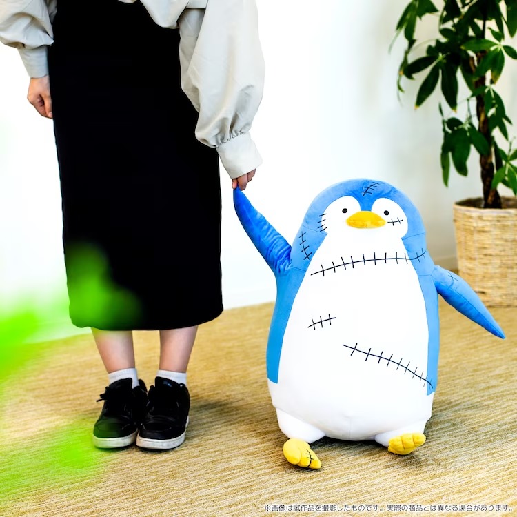 A promotional image of the SPY x FAMILY "Penguin Plush Toy" featuring the toy posed next to a model who is holding its flipper as if the two of them are going for a pleasant stroll together.