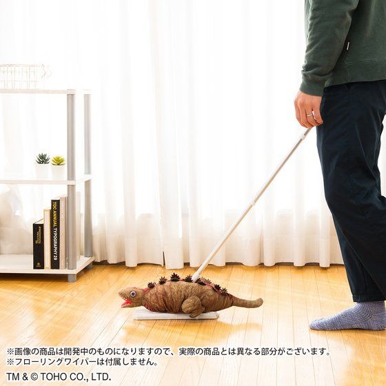 A promotional image of the Shin Godzilla 2nd Form Flooring Wiper Cover character good, depicting the product being used along with a flooring wiper to clean a Japanese style apartment floor.