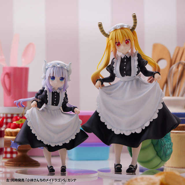 A promotional image for the Miss Kobayashi's Dragon Maid Tohru and Kanna figures from Union Creative featuring both figures posed side-by-side in a kitchen setting. The figures feature Kanna and Tohru in traditional black-and-white maid outfits, and both characters are performing a curtsy and lifting the edges of their aprons.