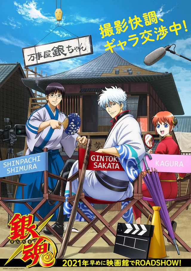 A "super teaser visual" for the newly announced Gintama theatrical anime film, featuring Shinpachi, Gintoki, and Kagura hanging out in director's chairs on the movie set of the Yorozuya Gin-chan building.