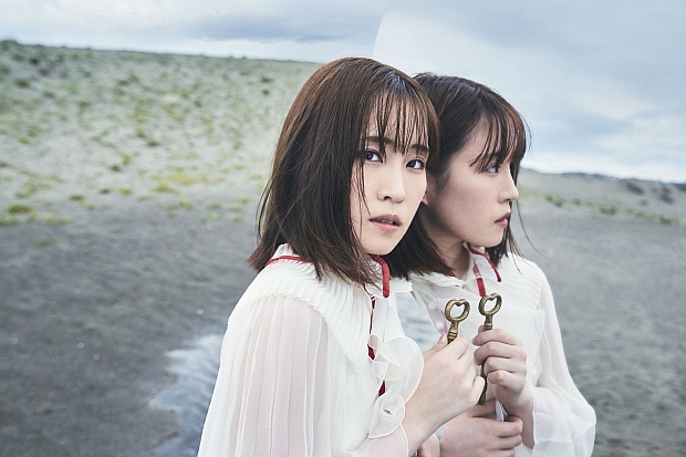 A promotional image featuring voice actor / singer Minori Suzuki posing with a key in front of a mirror on a beach with an anxious expression on her face.