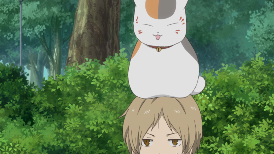 In his "beckoning cat" form, Nyanko-sensei flashes a smug expression and perches on top of Takashi Natsume's head in a scene from the sixth season of the Natsume Yujin-cho TV anime.