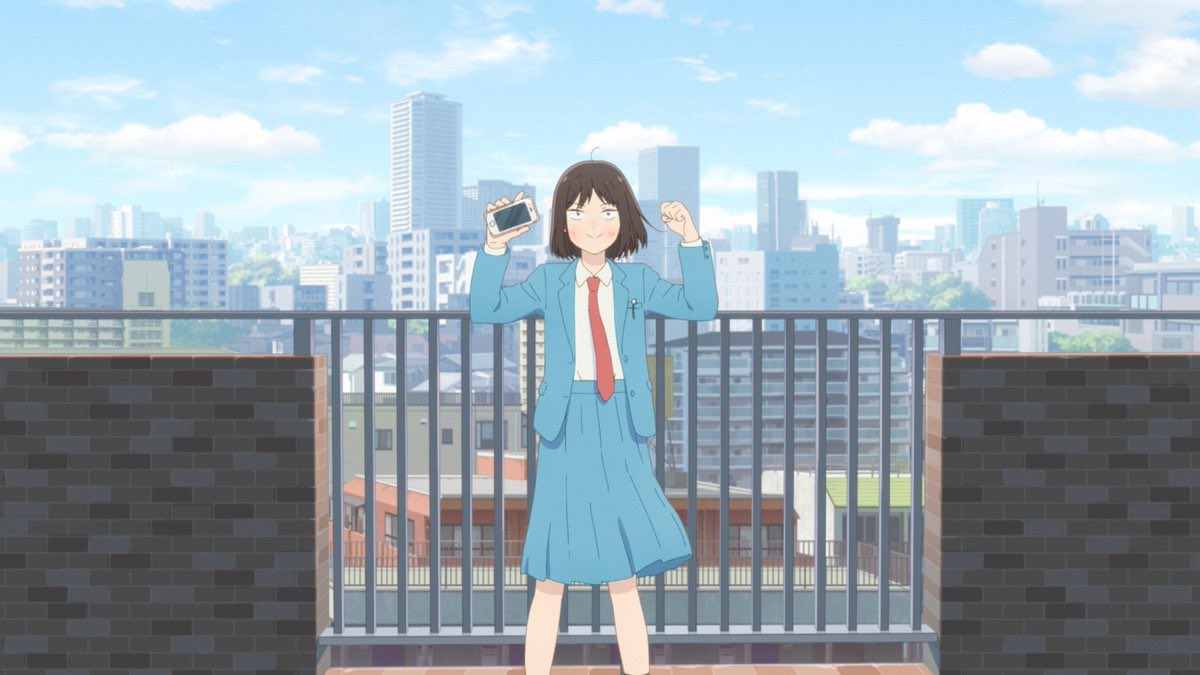 Vestida con su uniforme escolar, Mutsumi hace una pose de flexión de bíceps con su teléfono inteligente en una mano frente a la barandilla en el techo de su escuela secundaria en una escena del próximo anime de televisión Skip and Loafer.