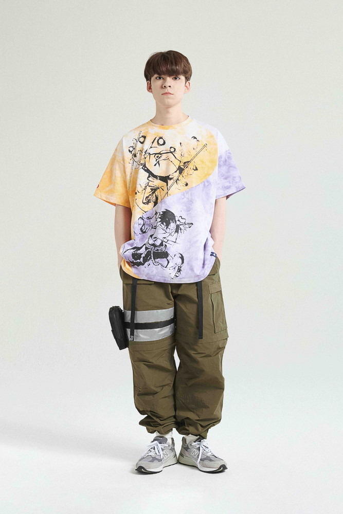 Ein junger Mann modelliert das RIVAL T-SHIRT und die 2-1 TACTICAL PANTS / KHAKI aus der Street Fashion-Zusammenarbeit LIBERE FOR NARUTO.