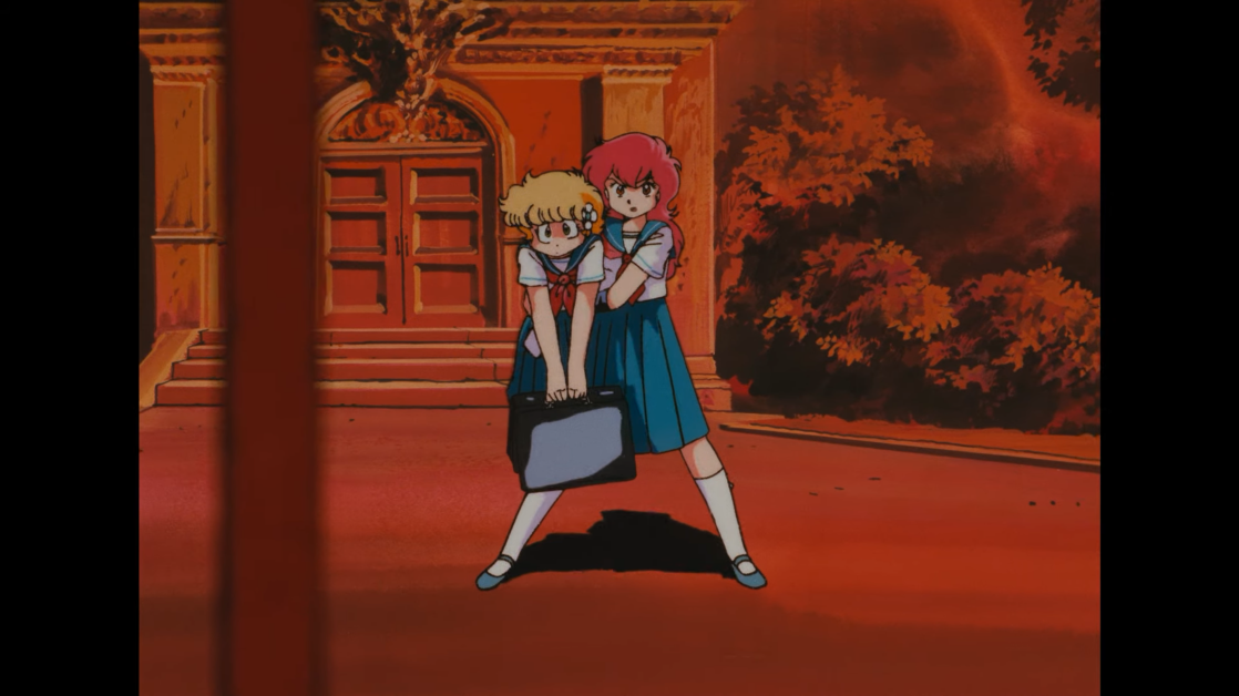 While carrying her best friend C-ko Kotobuki like a stuffed animal, perfectly ordinary Japanese high school girl scolds B-ko Daitokuji for ambushing her (again) with an arsenal of giant robots on the way to school in a scene from the 1986 Project A-ko theatrical anime film.