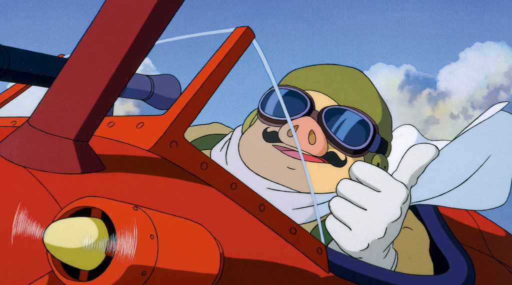 Porco Rosso, ein Flieger, der in ein humanoides Schwein verwandelt wurde, zeigt ein Daumen hoch-Zeichen und lächelt, während er sein Kampfflugzeug in einer Szene aus dem Porco Rosso-Kinoanimefilm von 1992 steuert.