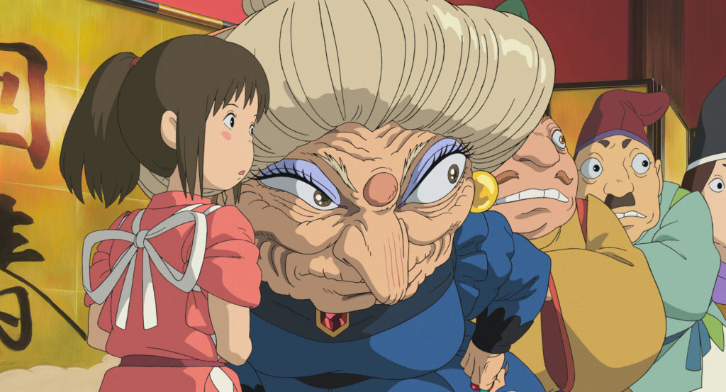Sen, Yubaba, and a gaggle of lollygaggers gather out front of the bath house in a scene from the 2001 theatrical anime film Spirited Away.
