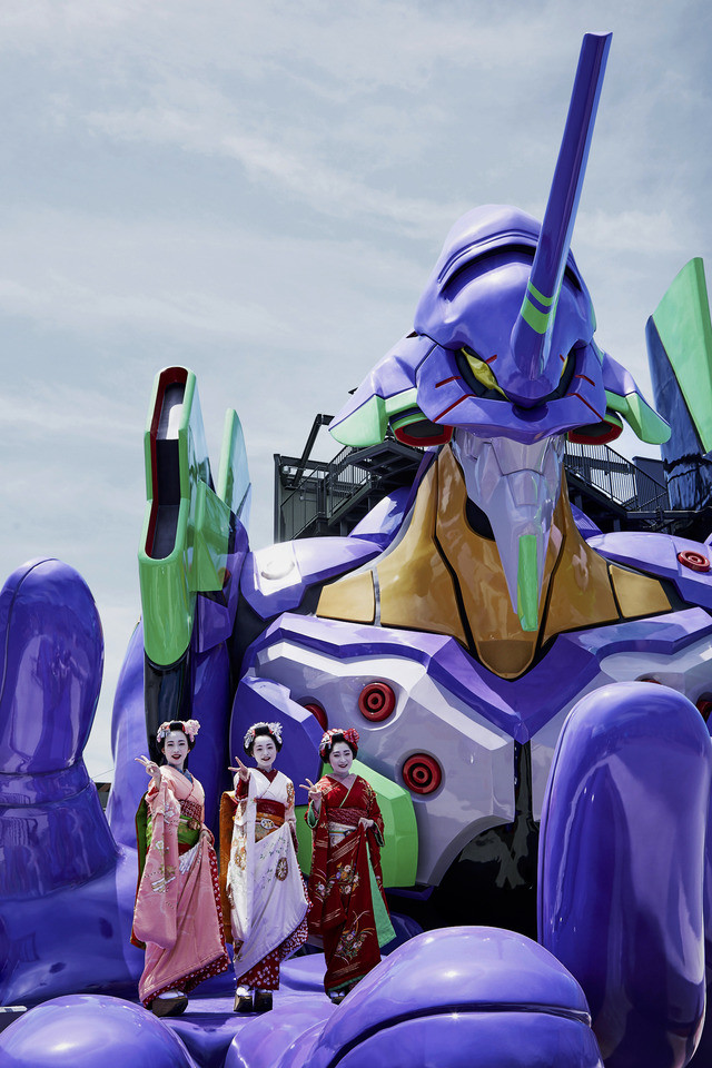 Three actresses dressed as geisha pose in the palm of Eva Unit-01's hand at the Evangelion Kyoto Base attraction at Toei Kyoto Studio Park.