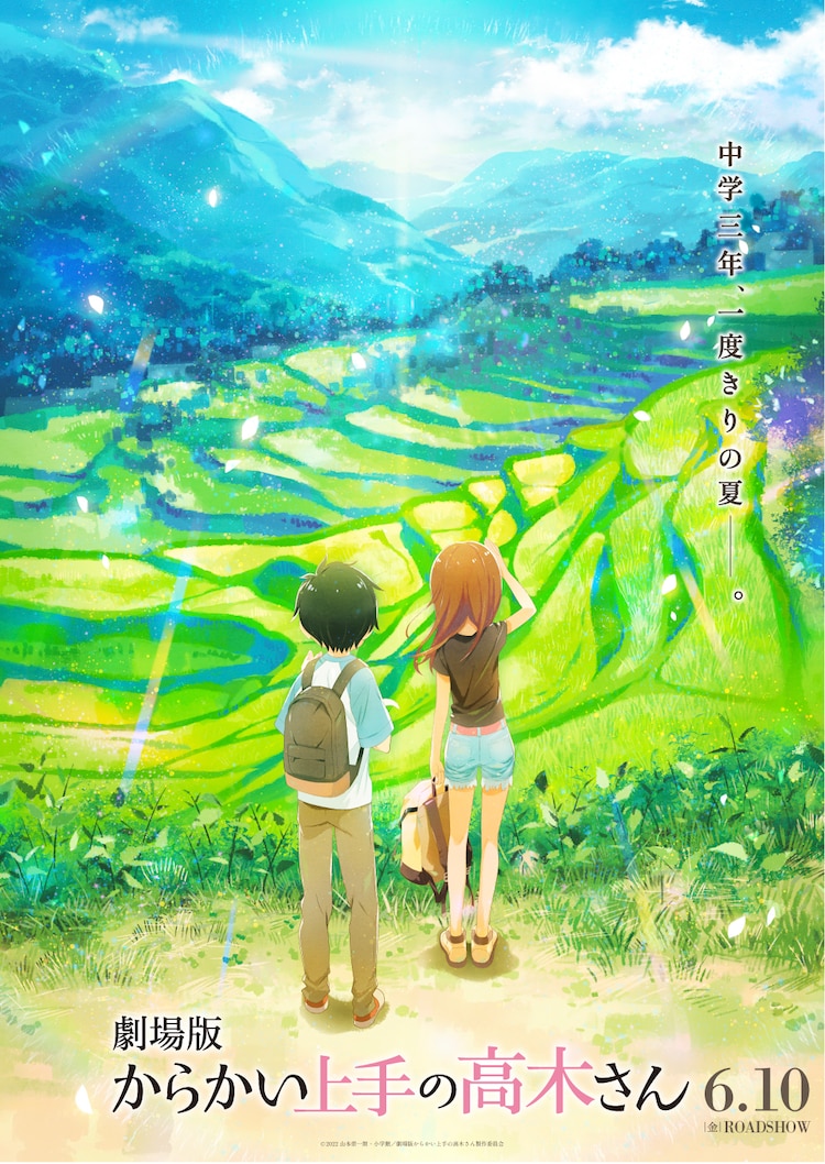 A teaser visual for the upcoming KARAKAI JOZU NO TAKAGI-SAN theatrical anime film featuring Nishikata and Takagi looking out over a series of rice paddies from an elevated position in the Japanese countryside. Nishikata and Takagi are dressed in summer clothes and have their backs to the camera.
