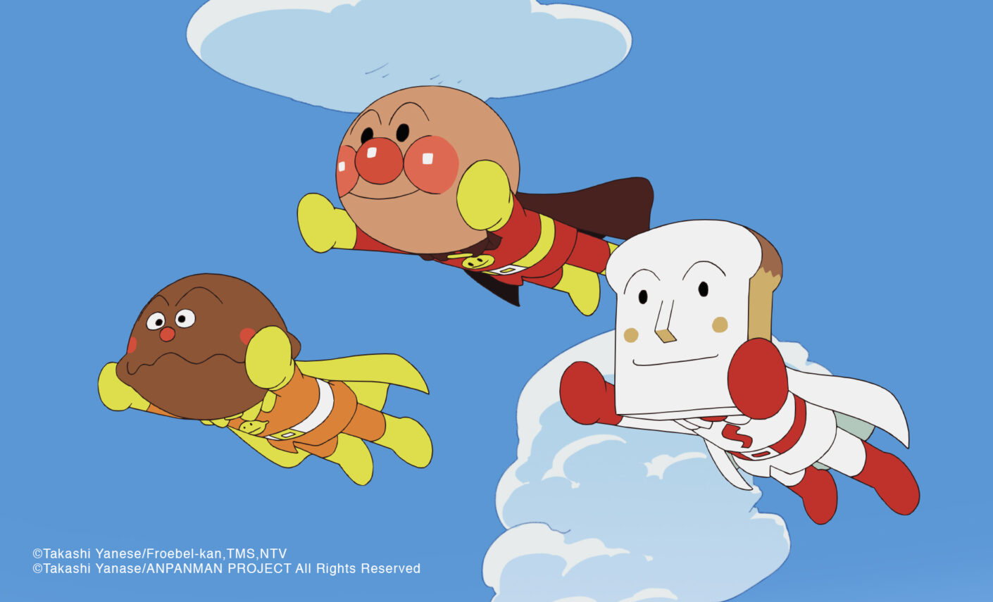 Ein Werbebild für die Anpanman-Anime-Serie mit dem Titelcharakter und zwei seiner brotköpfigen Freunde, die in ihren Superheldenkostümen durch den Himmel schweben.