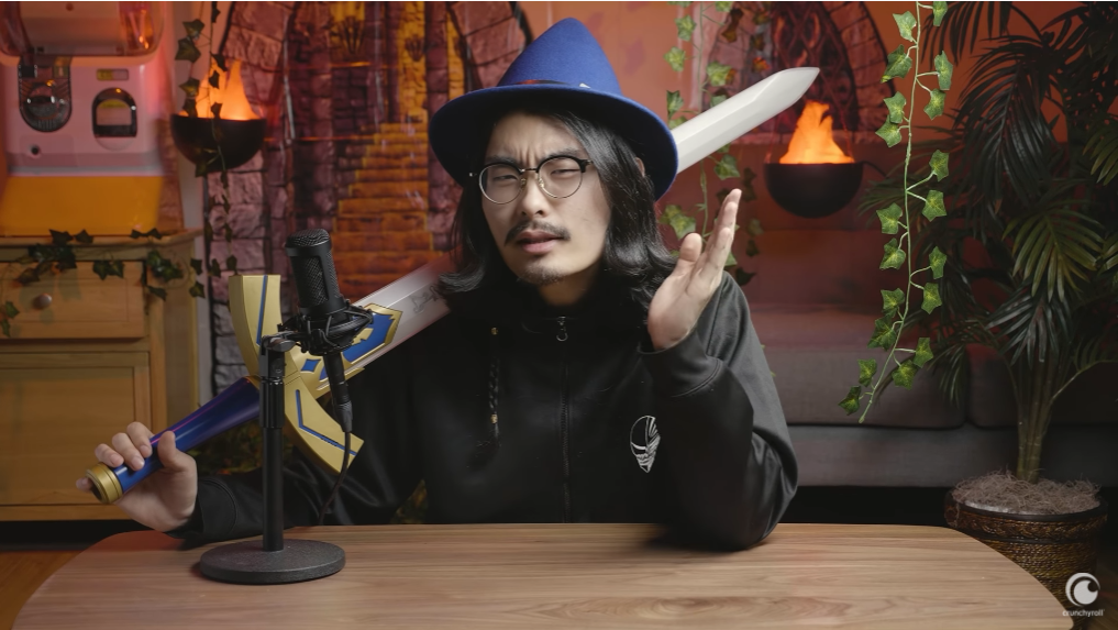 Tim Lyu dons a wizard had and brandishes the Master Sword from the Legend of Zelda video game series as he explains the history of isekai anime in front of a backdrop designed to look like a fantasy dungeon in a scene from the Anime Explained Youtube video essay series.